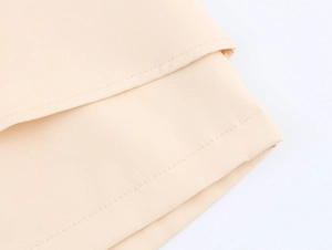 Close-up of beige woven fabric texture and neat double-row stitching on asymmetric shorts
