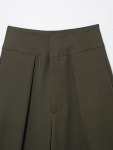Detail of high waisted dark olive trousers showing pleated design and woven texture