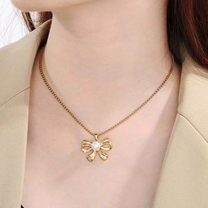 Close-up of a golden bow pendant with white pearl on a delicate layered chain