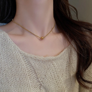 Detail of a minimalist gold bead pendant necklace worn by a model on a beige background