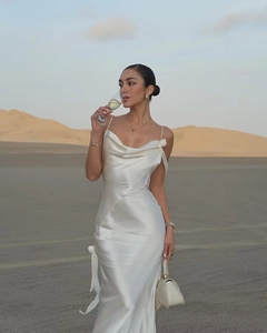 Elegant white satin slip dress with cowl neck and flowing ribbon detail in desert sunset
