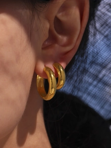 Close-up of chunky gold hoop earrings with polished reflective finish on a model