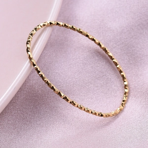 Close-up of golden geometric bangle with rhombus textures on pink satin fabric