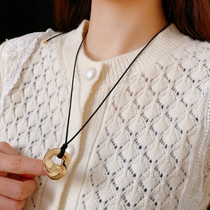 Detail of a minimalist gold irregular metal ring pendant on a black cord necklace