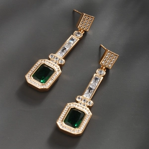 Macro detail of gold vintage earrings with emerald green gems and white zircon inlay