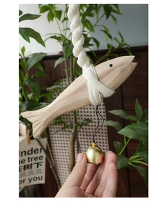 Detail of wooden fish hanging decor with thick cotton rope and gold metal bell