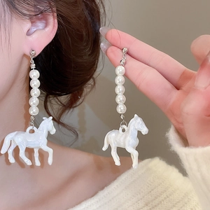Détail de boucles d'oreilles cheval en résine avec chaîne de perles sur un modèle