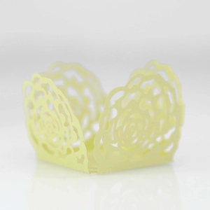 Detail of laser-cut pale yellow cupcake wrapper featuring intricate rose lace patterns
