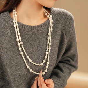 Detailed view of layered white pearl necklace worn on a grey sweater for a French chic style