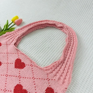 Detail of pink knitted tote bag with red heart patterns on white waffle fabric