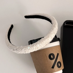 Detail view of white plush sequin headband resting on a coffee cup with stylish texture