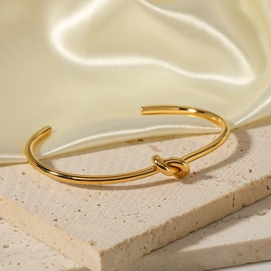 Minimalist 18K gold plated stainless steel knot cuff bracelet on elegant stone stand
