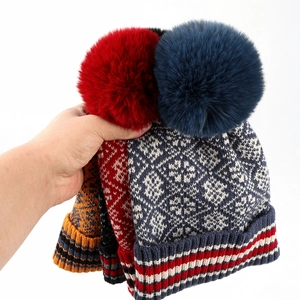 Detail of knitted winter hats with snowflake patterns and large faux fur pom-poms