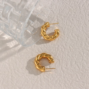 Close-up of golden twisted rope C-shaped hoop earrings on a minimalist white texture