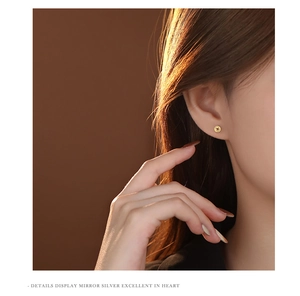 Close-up of golden coin-shaped sterling silver stud earrings on a model's ear