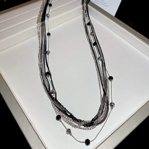 Close-up of layered black and silver beaded necklace on a gray display tray
