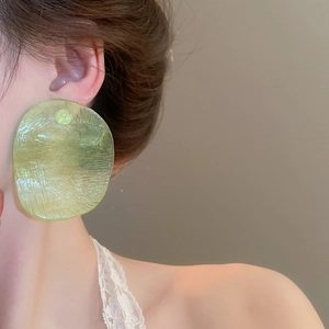 Close-up of oversized light green textured resin earrings worn by a model in profile
