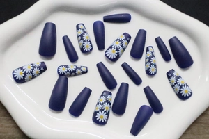 Detail of matte navy blue press-on nails with white daisy floral prints on ceramic tray