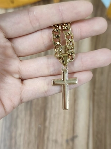 Detailed view of hand holding a golden punk style stainless steel cross pendant Cuban chain
