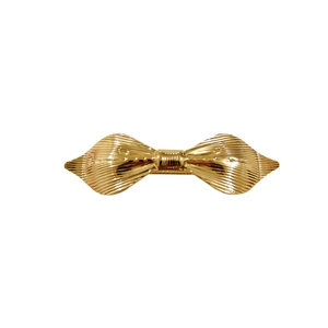 Detail of a minimalist gold metal bow hair clip showing textured stripes and polished finish
