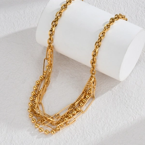Minimalist multi-layered gold necklace with bead and paperclip chains on a white stand