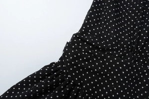 Vista macro di pois bianchi su tessuto in chiffon nero con trama a pieghe fitte