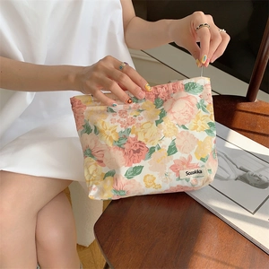 Detail of floral cotton makeup bag held by hand, showing textured fabric and zipper