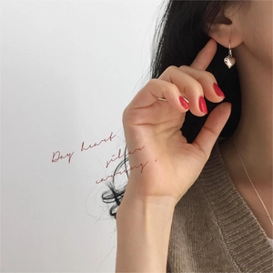Macro shot of silver heart drop earrings worn by a model with elegant knitwear