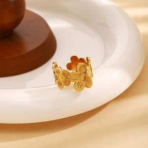 Gold hollow floral stainless steel open ring with matte textured petals on a ceramic tray