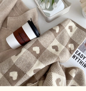 Detail of a brown and cream checkered knit scarf with woven heart patterns and warm texture