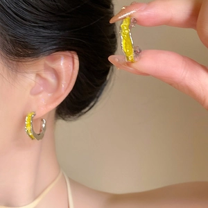 Détail de créoles argentées en forme de C avec émail jaune et finition métal texturé