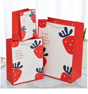 Three sizes of red strawberry paper gift bags stacked in a clean home setting