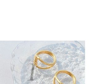 Detail of minimalist gold-plated twisted rope rings with intricate texture on glass tray