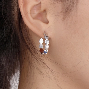 Close-up of a silver heart-shaped hoop earring worn by a model in bright lighting
