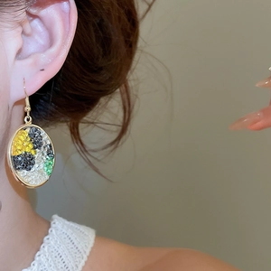 Close-up of a gold oval drop earring with colorful mosaic beads worn by a model