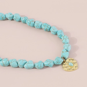 Detail of bohemian turquoise beaded necklace with gold heart-shaped pendant and hammered finish