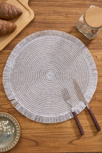Detail of silver round woven placemat with elegant fringe on a rustic wooden table