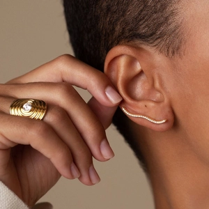 Macro detail of wave-shaped zircon earrings and wide threaded gold ring on skin