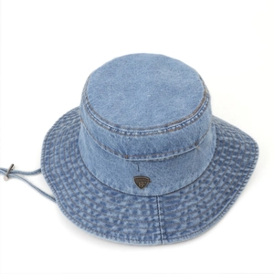 Detail of light blue denim bucket hat with metal logo badge and adjustable chin strap