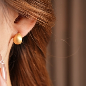 Close-up of a minimalist gold teardrop earring with a matte brushed finish on model