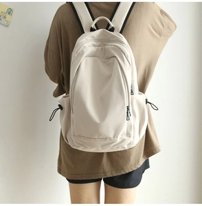 Detailed back view of a minimalist cream-white large capacity backpack worn by a model