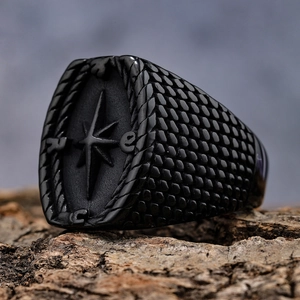 Macro detail of men's matte black compass ring with textured sides on a wood surface