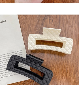 Detail of black and white quilted lattice hair claws on a minimalist wooden surface