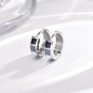 Close-up of stainless steel huggie earrings with black grey and white enamel geometric patterns