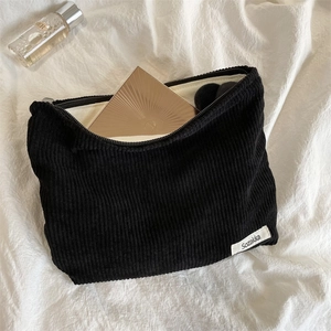 Detail of black corduroy makeup bag texture with brand label on soft white fabric background