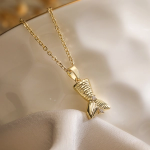 Elegant gold fish tail necklace with crystals on soft fabric background