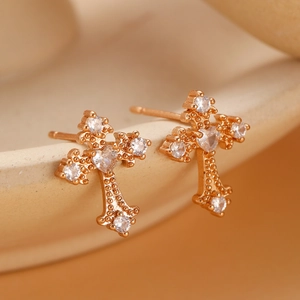 Detail of rose gold cross earrings with heart-shaped zircon on beige ceramic bowl