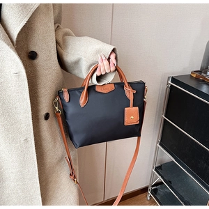 Close-up of black nylon tote bag with brown leather handles and a leather brand patch