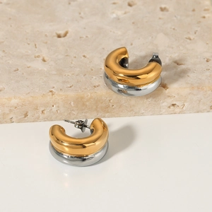 Two-tone gold and silver C-shaped chunky hoop earrings on a textured stone surface