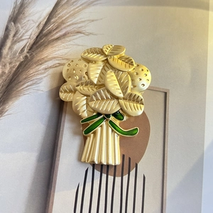 Détail d'une broche bouquet de feuilles dorées mates avec ruban émaillé vert sur fond artistique